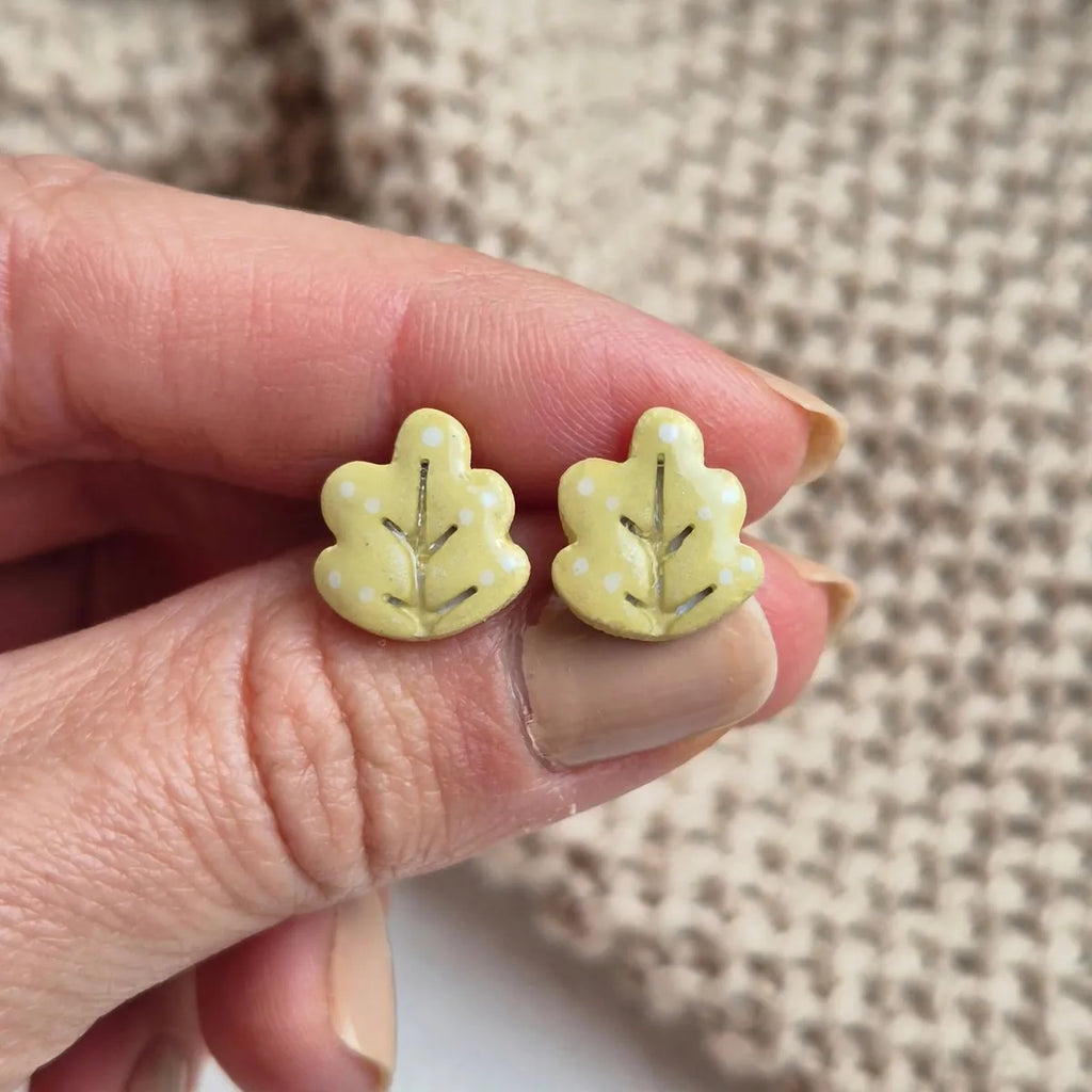 Deux puces d’oreilles feuille de chêne tenues entre les doigts pour montrer leur taille