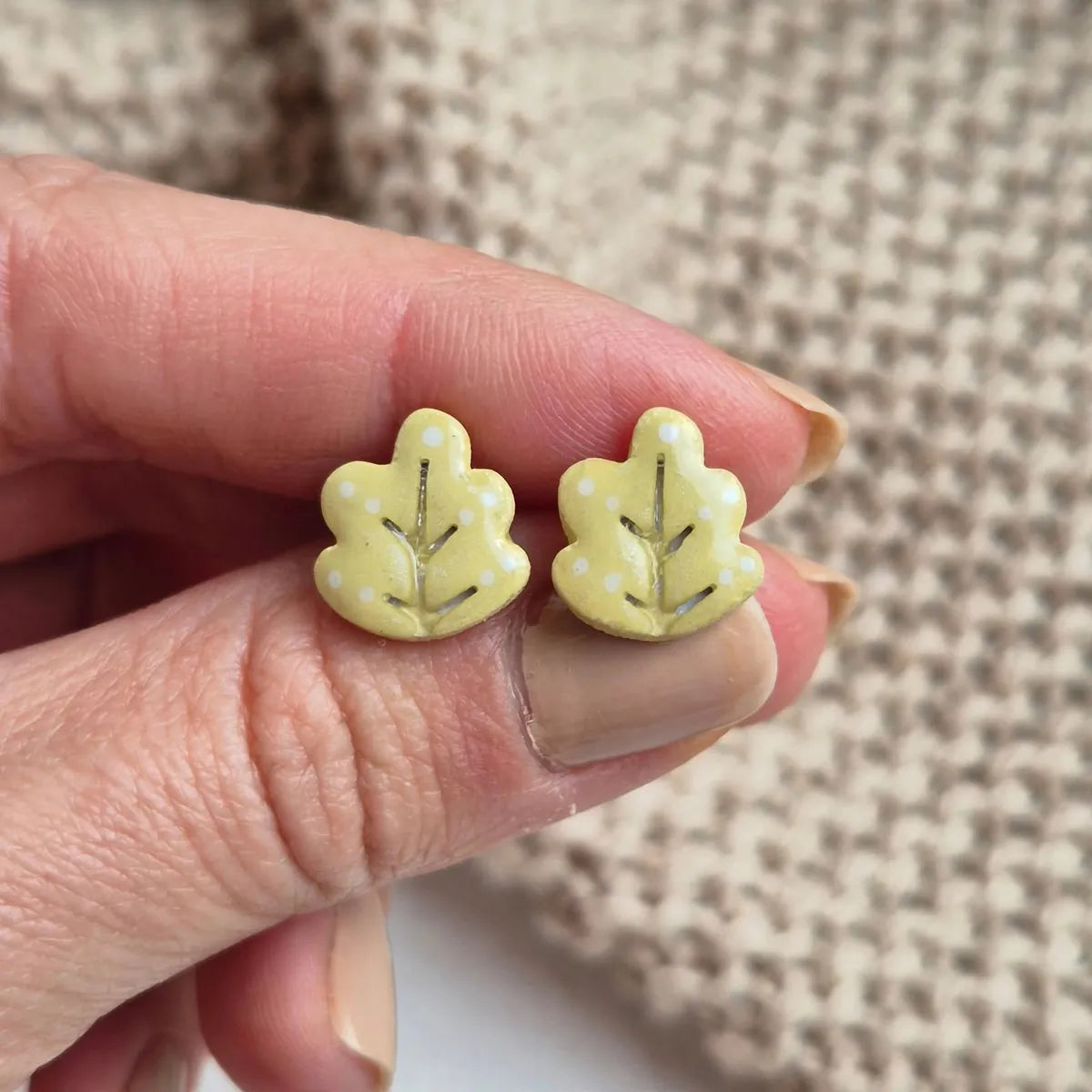 Deux puces d’oreilles feuille de chêne tenues entre les doigts pour montrer leur taille