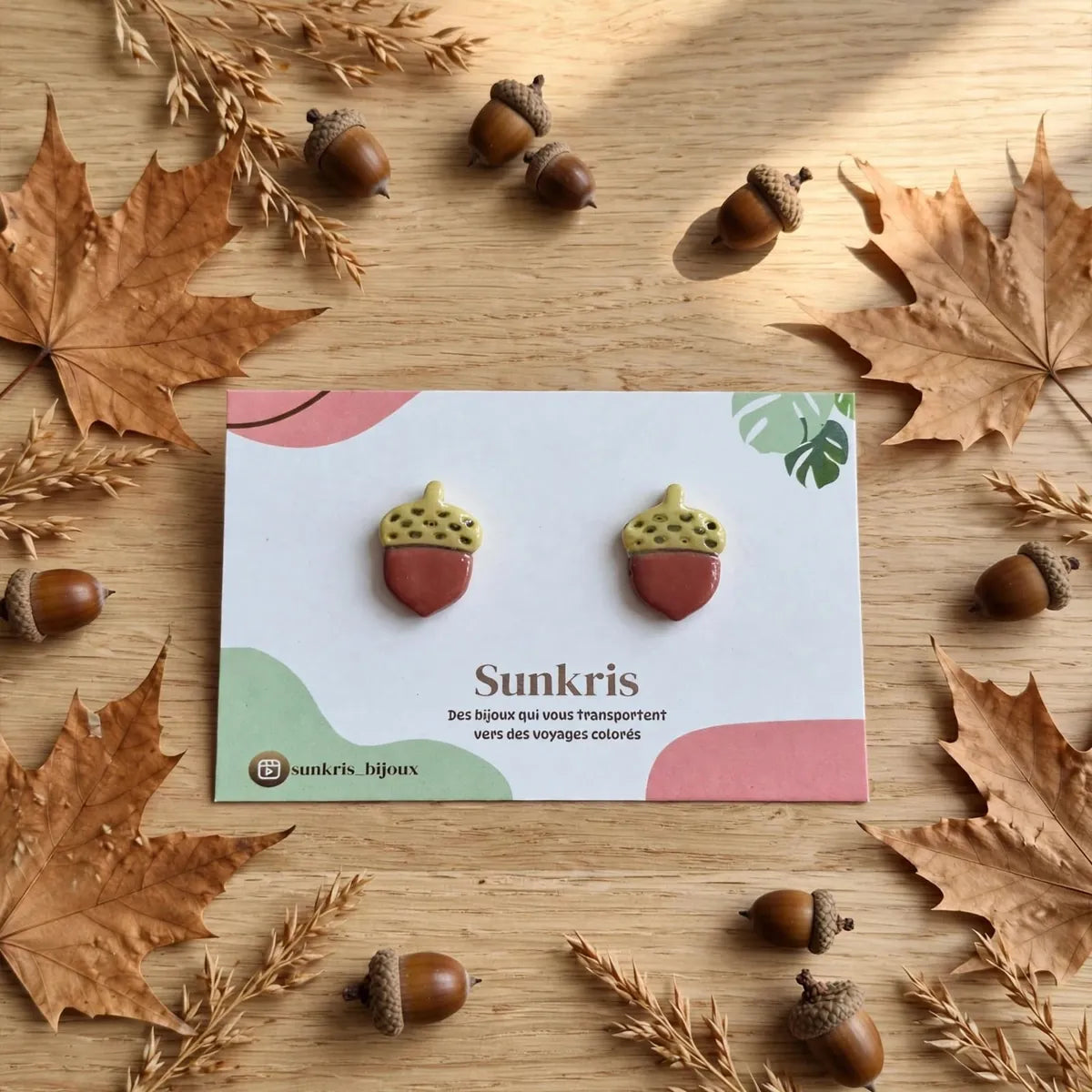 Paire de puces d’oreilles gland sur une carte Sunkris entourée de feuilles et de glands d’automne 