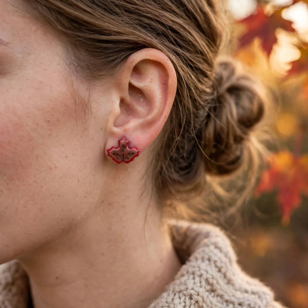Puce d’oreille feuille d’érable rouge portée à l’oreille avec un pull en maille claire