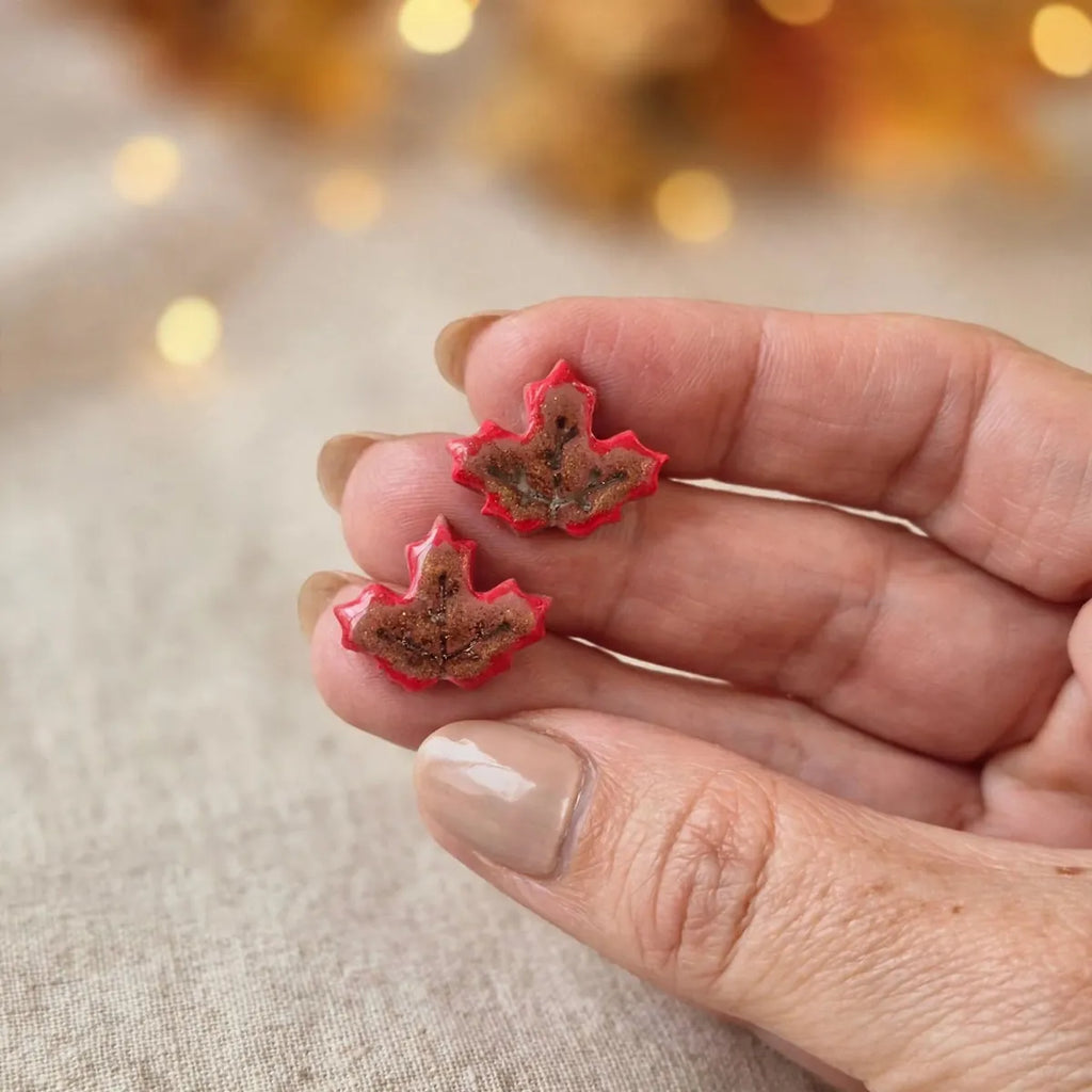 Deux puces d’oreilles feuille d’érable rouge tenues entre les doigts pour montrer leur taille