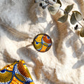 Bague wax orange et bronze Sunkris posée sur textile beige, décor d'eucalyptus