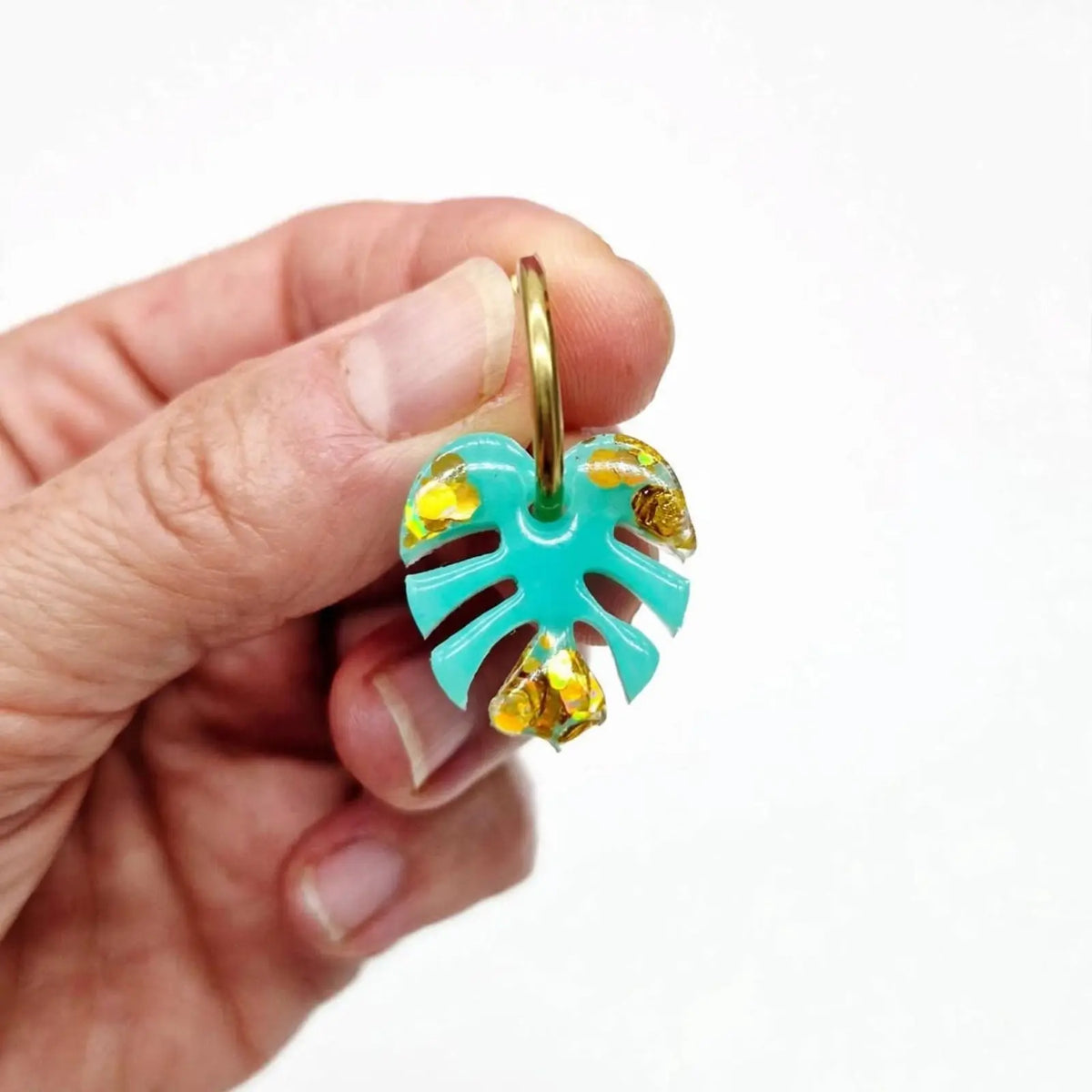 Boucle d'oreille créole feuille de monstera turquoise et paillettes dorées tenue en main - bijou fantaisie SunKris