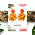 Boucles d'oreilles fruit de la passion Sunkris sur carte de présentation, posées sur bois flotté