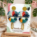 Boucles d'oreilles galet tropical monstera Sunkris sur carte de présentation, socle bois