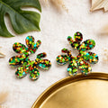 Boucles d'oreilles marguerite pailletée verte Sunkris posées sur lin beige, décor de feuille et plateau doré