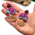 Une main présente la paire de boucles d'oreilles ginkgo en wax violet signée Sunkris