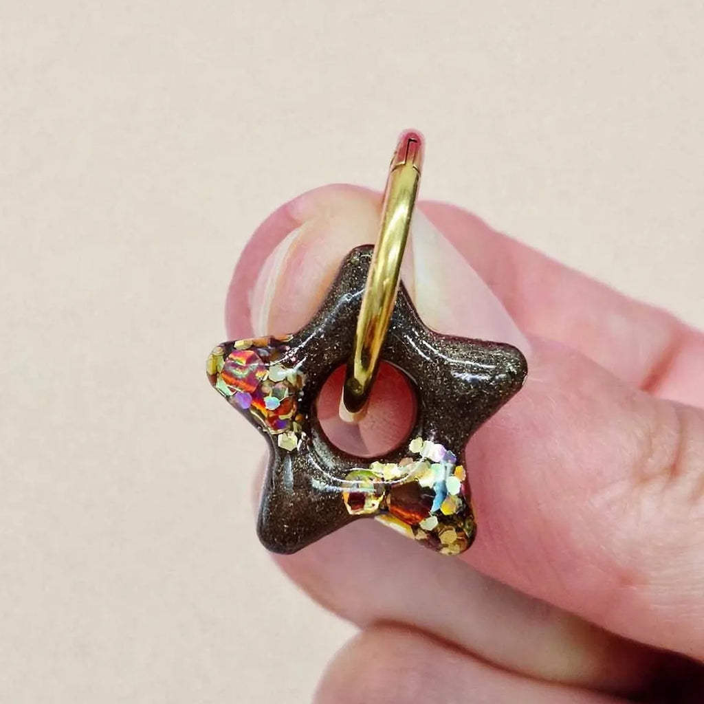 Gros plan d'une boucle d'oreille étoile en résine marron et paillettes holographiques tenue entre les doigts