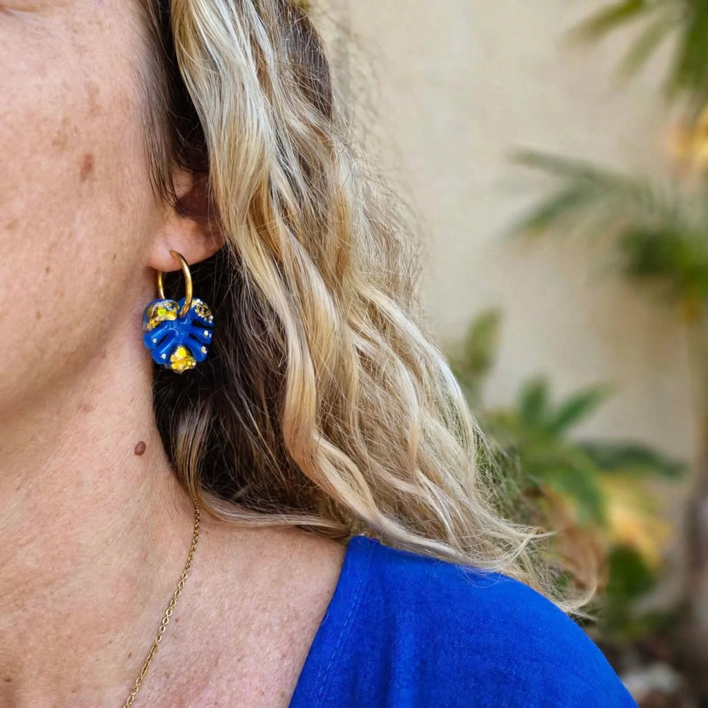 Boucles d'oreilles créole feuille de monstera bleue et or Sunkris portées, gros plan