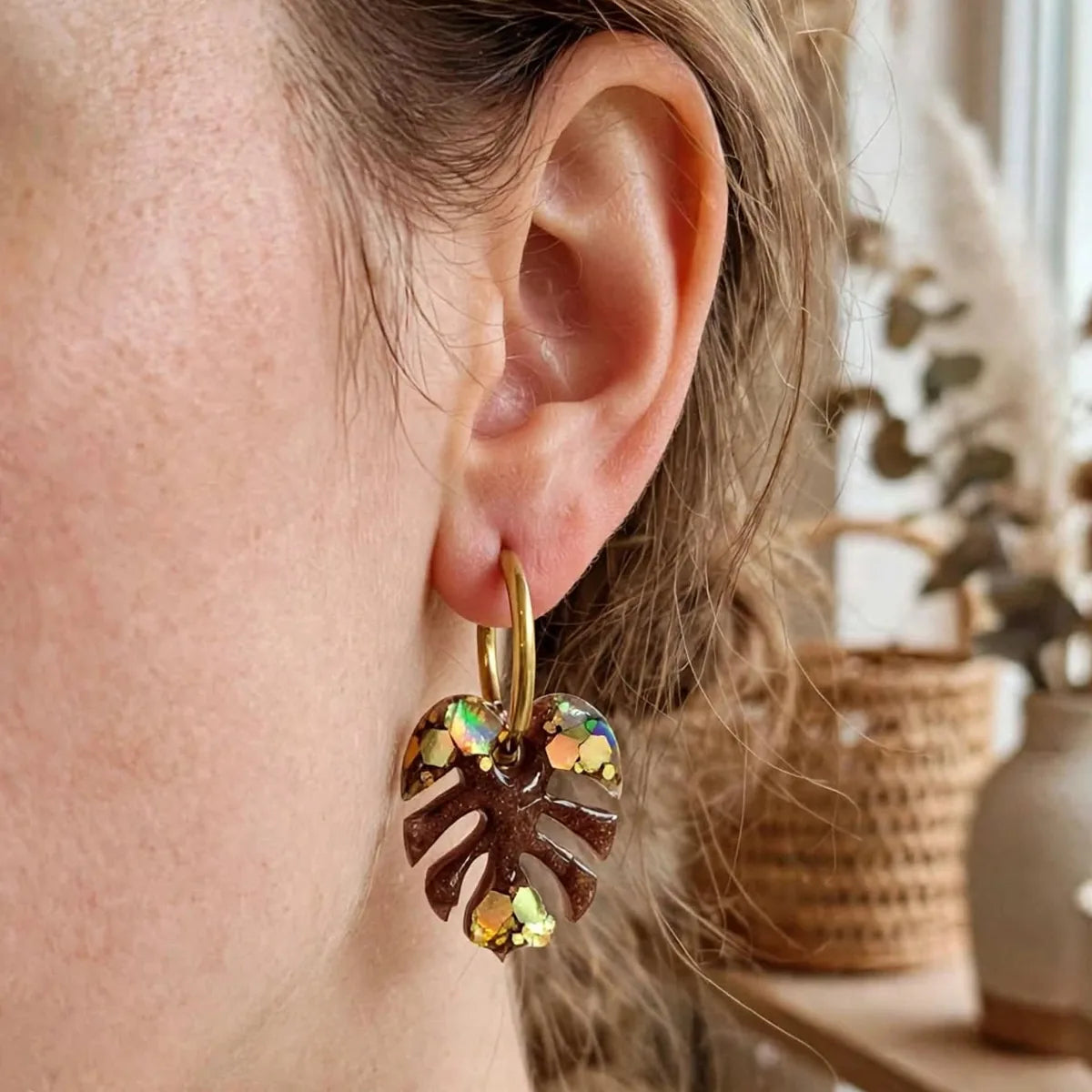 Boucle d'oreille feuille de monstera en résine marron et paillettes dorées, créole dorée, portée à l'oreille