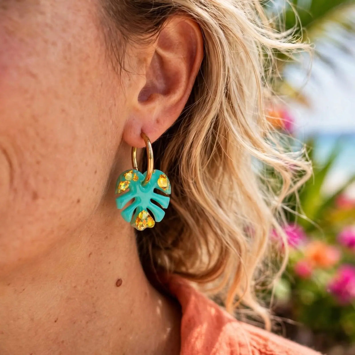 Boucle d'oreille créole feuille de monstera turquoise portée à l'oreille, gros plan sur le bijou