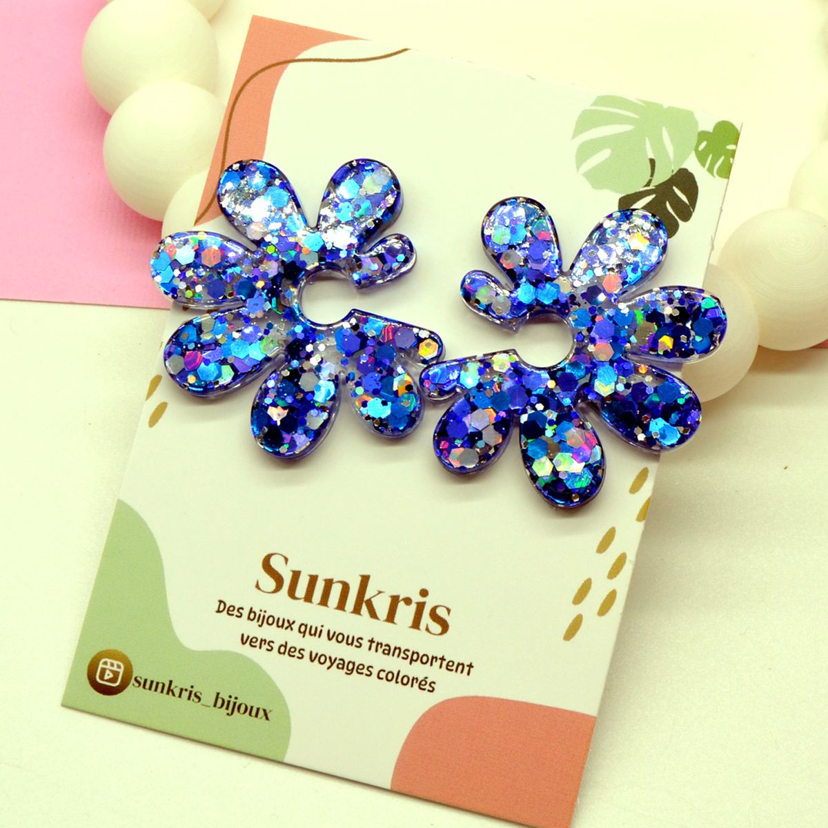 Boucles d’oreilles fleur bleu holographique en résine présentées sur la carte Sunkris, bijoux faits main