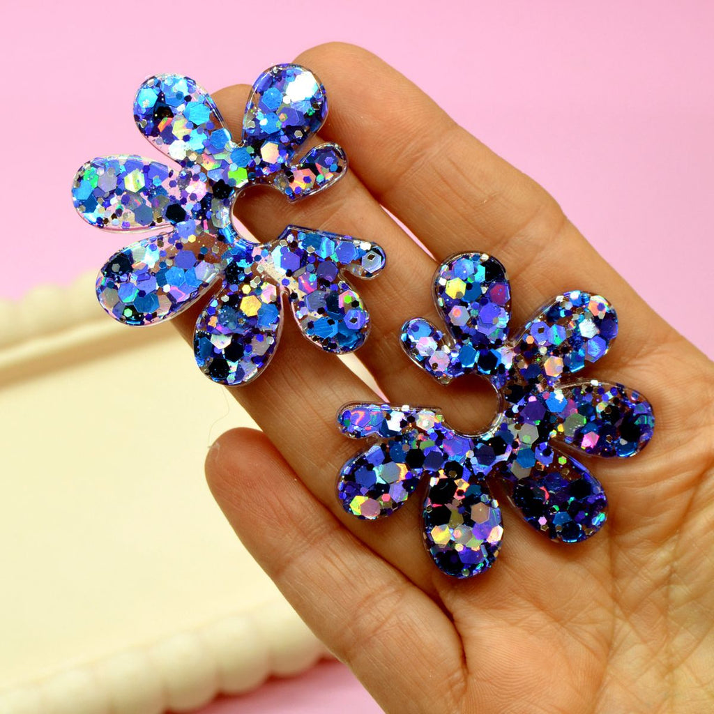 Taille des boucles d’oreilles fleur en résine à paillettes bleues holographiques comparée à une main