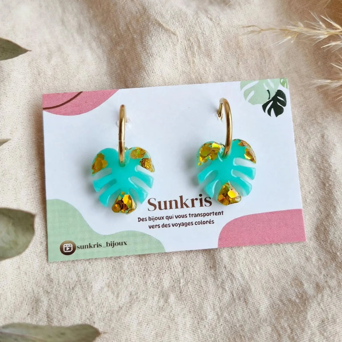 Boucles d'oreilles créoles feuille de monstera turquoise et paillettes dorées sur carte de présentation Sunkris