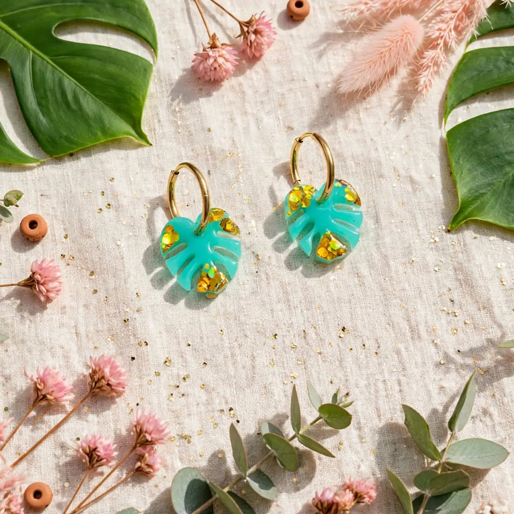 Boucles d'oreilles feuille de monstera turquoise en mise en scène tropicale avec feuilles et fleurs séchées