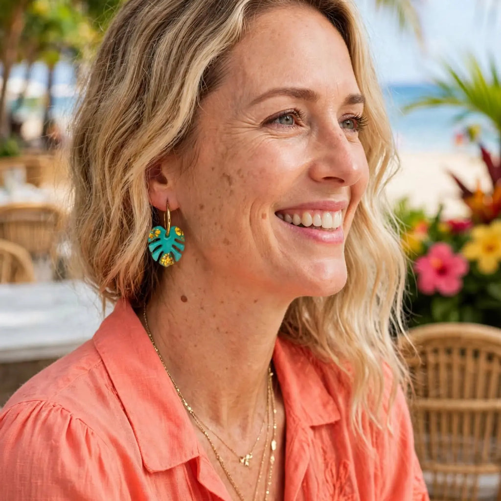 Femme souriante portant des boucles d'oreilles feuille de monstera turquoise, ambiance tropicale bord de mer