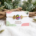 Bracelet abstrait cabochon coloré Sunkris avec sa carte de présentation, posé sur bois flotté
