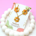 Parure fleur orange Sunkris présentée sur carte de marque, posée sur perles blanches